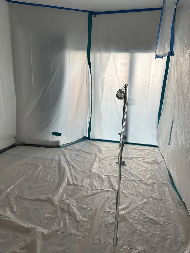 Plastic-sheet containment walls and protected floor with a small instrument mounted on a stand.