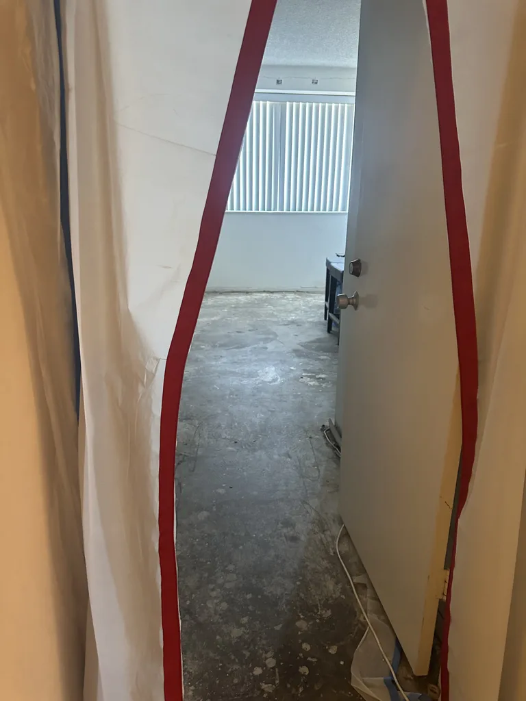 Open red-zippered plastic containment doorway leading into a room with an exposed floor.
