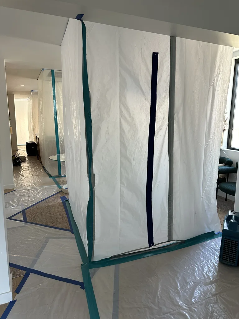 Freestanding plastic containment enclosure with dark vertical zipper and taped floor protection.